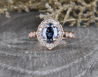 May include: A rose gold engagement ring with a gray oval-shaped center stone surrounded by a halo of smaller diamonds. The ring has a delicate, intricate design with a floral motif.