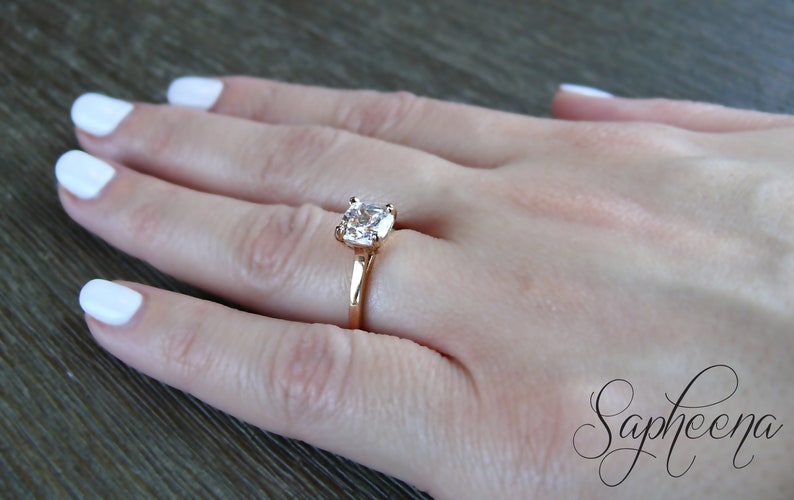 May include: A rose gold ring with a large, clear, square-shaped gemstone.