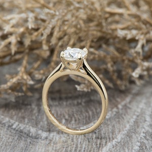 May include: A gold solitaire engagement ring with a round brilliant cut diamond. The ring has a simple, elegant design with a thin band.