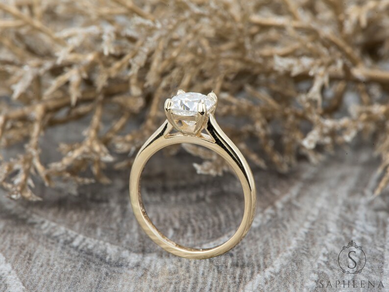 May include: A gold solitaire engagement ring with a round brilliant cut diamond. The ring has a simple, elegant design with a thin band.