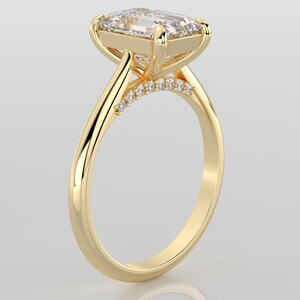 May include: A gold engagement ring with a large, clear, square-shaped diamond set in a prong setting. The band is thin and has a row of smaller diamonds set in a pave setting.