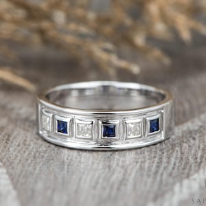 Op de afbeelding: Een zilveren bandring met een rij afwisselend vierkante blauwe saffieren en heldere diamanten.