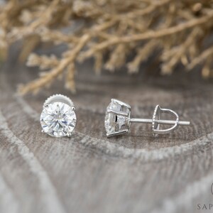 May include: A pair of silver stud earrings with large, round, clear gemstones. The earrings have a screw-back closure.