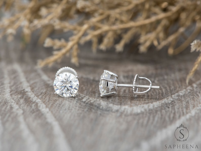May include: A pair of silver stud earrings with large, round, clear gemstones. The earrings have a screw-back closure.
