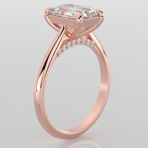 May include: A rose gold engagement ring with a large, clear, square-shaped diamond set in a prong setting. The band is thin and has a row of smaller diamonds set in a pave setting.
