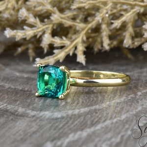Op de afbeelding: Een gouden ring met een vierkante smaragdgroene edelsteen.