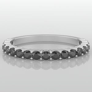 Puede incluir: Un anillo de banda de plata con una fila de piedras redondas negras.
