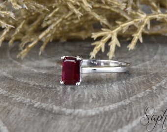 May include: A silver ring with a red emerald-cut gemstone.