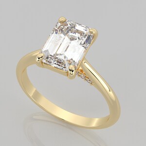 May include: A gold engagement ring with a large, clear emerald-cut diamond. The band is set with smaller diamonds on the side.