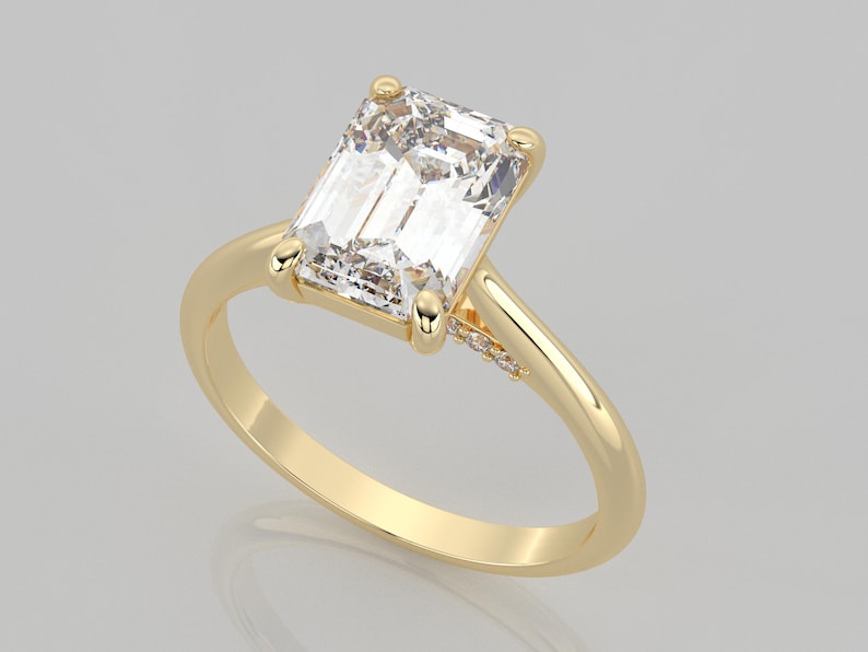 May include: A gold engagement ring with a large, clear emerald-cut diamond. The band is set with smaller diamonds on the side.
