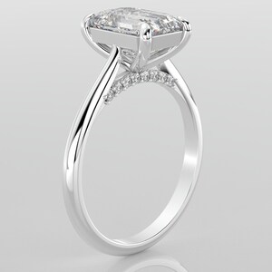May include: A silver engagement ring with a large, clear, square-shaped diamond set in a prong setting. The band is thin and has a row of smaller diamonds set in a pave setting.