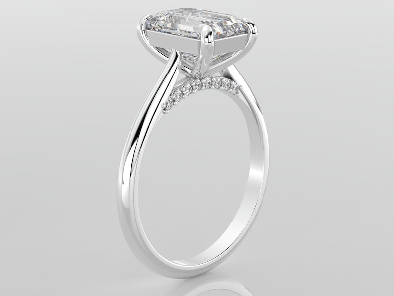 May include: A silver engagement ring with a large, clear, square-shaped diamond set in a prong setting. The band is thin and has a row of smaller diamonds set in a pave setting.
