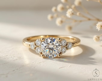 Op de afbeelding: Een gouden ring met een grote, ronde, heldere edelsteen als middelpunt, omringd door kleinere, heldere edelstenen. De ring heeft een delicaat, elegant ontwerp, met een gepolijste afwerking. De ring staat tegen een zachte, neutrale achtergrond.