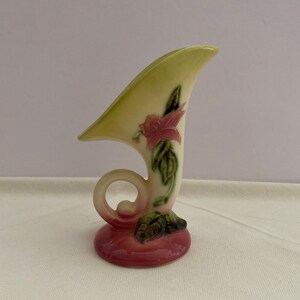 Può includere: Un vaso vintage in ceramica a forma di corno con un fiore rosa e foglie verdi dipinte sul lato. Il vaso ha una smaltatura color crema con una base rosa.