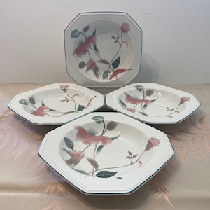 Peut inclure: Ensemble de quatre bols octogonaux blancs avec un motif floral. Les bols pr&eacute;sentent un motif floral rose et vert avec une bordure bleu fonc&eacute;. Les bols sont dispos&eacute;s sur une surface de couleur claire.