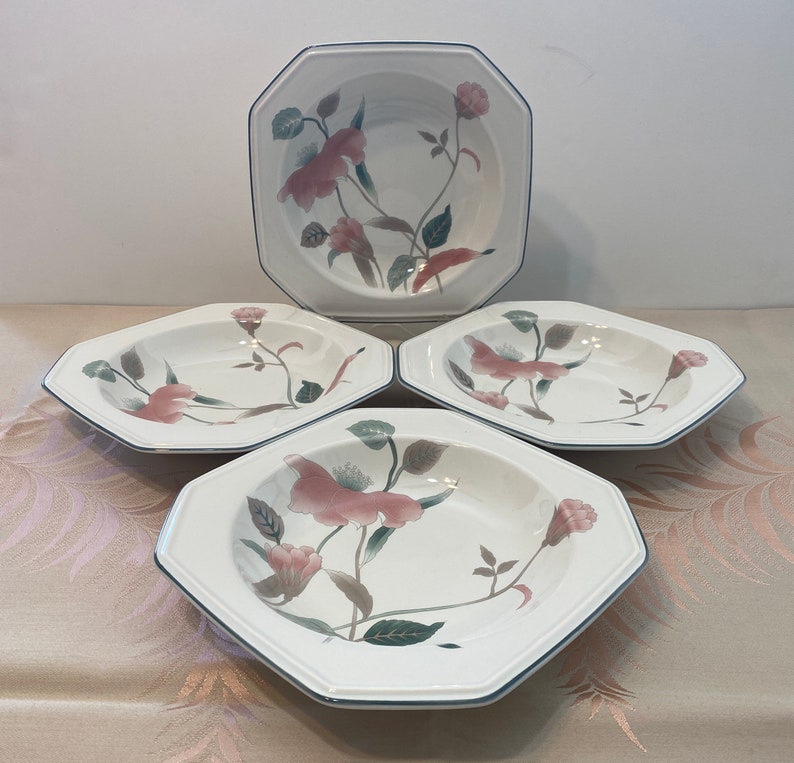 Peut inclure: Ensemble de quatre bols octogonaux blancs avec un motif floral. Les bols pr&eacute;sentent un motif floral rose et vert avec une bordure bleu fonc&eacute;. Les bols sont dispos&eacute;s sur une surface de couleur claire.