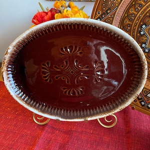 Peut inclure: Un plat de service ovale en céramique brun et blanc avec un motif en relief. Le plat est sur un support en métal doré.