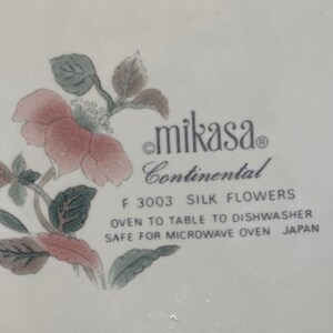 Peut inclure: Vaisselle blanche Mikasa Continental avec un motif floral. Le motif pr&eacute;sente des fleurs roses et rouges avec des feuilles vertes. Le texte "F 3003 SILK FLOWERS" est visible, ainsi que "OVEN TO TABLE TO DISHWASHER SAFE FOR MICROWAVE OVEN JAPAN."