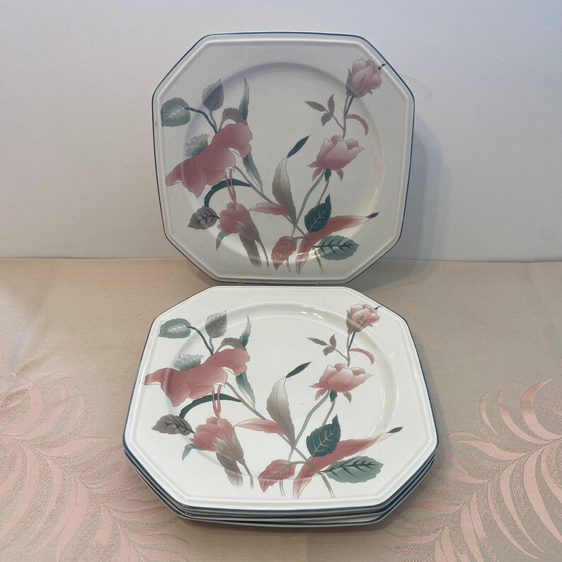 Peut inclure: Ensemble d'assiettes blanches octogonales avec un motif floral de roses roses et de feuilles vertes. Les assiettes ont une bordure bleu fonc&eacute;. Les assiettes sont empil&eacute;es.