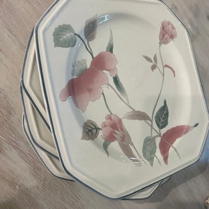 Peut inclure: Une pile d'assiettes blanches octogonales avec un motif floral. Les assiettes pr&eacute;sentent des fleurs roses et marron clair avec des feuilles vertes et un bord bleu. Les assiettes sont empil&eacute;es sur une surface en bois clair.
