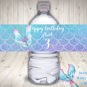 Peut inclure: Étiquette de bouteille d'eau avec un motif de queue de sirène et le texte "Happy Birthday Ariel 3". L'étiquette a un fond iridescent bleu et violet avec un motif de queue de sirène.