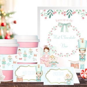 Peut inclure: Deux gobelets en papier roses avec un motif de Casse-Noisette et de ballerine. Une pancarte indique "Réchauffez-vous au bar à chocolat chaud".