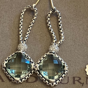 Pode incluir: Brincos pendurados em prata com uma pedra preciosa verde quadrada e facetada. Os brincos apresentam um design de corrente e um pequeno detalhe redondo cravejado de diamantes. Os pinos dos brincos são dourados.