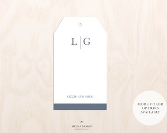 May include: A white gift tag with a blue border and the initials "L|G" in blue. The text "Lizzie and Greg" is printed below the initials. The tag has a hole at the top for string or ribbon. The text "More color options available" is printed on a white circle below the tag.