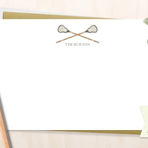 May include: A white card with a brown envelope. The card has a drawing of two lacrosse sticks crossed over each other. The text "TIM BURTON" is printed below the sticks. A small green and white tag is in the lower right corner with the text "MORE COLORS AVAILABLE!"