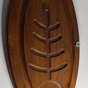 May include: Oval wooden serving tray with a carved tree design. The tray has a dark brown finish, two curved handles, and a metal fastener. The tree design is carved into the center of the tray.