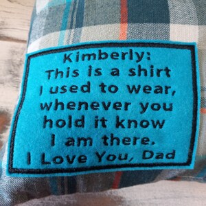 May include: A cushion with a blue and grey plaid pattern. A turquoise patch with black text reads: "Kimberly: This is a shirt I used to wear, whenever you hold it know I am there. I Love You, Dad."