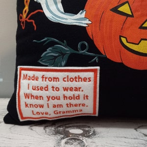 May include: Black Halloween-themed pillow featuring a smiling orange pumpkin and a white ghost illustration. The pillow includes a patch with the text: "Made from clothes I used to wear. When you hold it know I am there. Love, Gramma."
