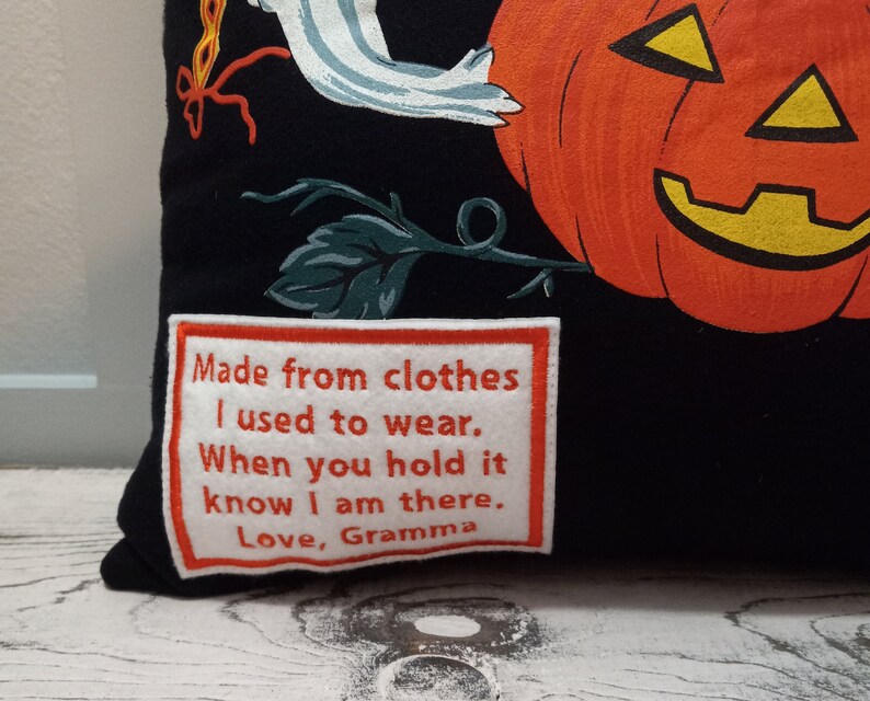 May include: Black Halloween-themed pillow featuring a smiling orange pumpkin and a white ghost illustration. The pillow includes a patch with the text: "Made from clothes I used to wear. When you hold it know I am there. Love, Gramma."