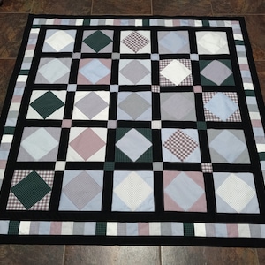 May include: A handmade quilt with a grid pattern of alternating squares and diamonds. The squares are black, and the diamonds feature various colors and patterns, including white, blue, green, and red gingham. The quilt has a black border and a decorative edge.
