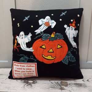 May include: Black Halloween-themed pillow featuring a large orange jack-o'-lantern with a smiling face, surrounded by three cartoon ghosts, bats, and stars. A patch with text reads "Made from clothes I used to wear. When you hold it know I am there. Love, Gramma."
