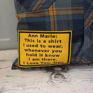 May include: A cushion made from a blue and gold plaid shirt. A yellow patch with black embroidered text reads: "Ann Marie: This is a shirt I used to wear, whenever you hold it know I am there. I Love You, Dan."