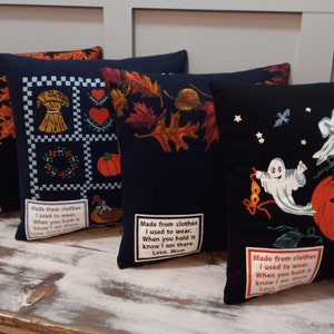 May include: Four decorative throw pillows with fall and Halloween themes. Designs include autumn leaves, a harvest scene, and ghosts with a jack-o'-lantern. Each pillow has a black background and a sewn-on label with text.