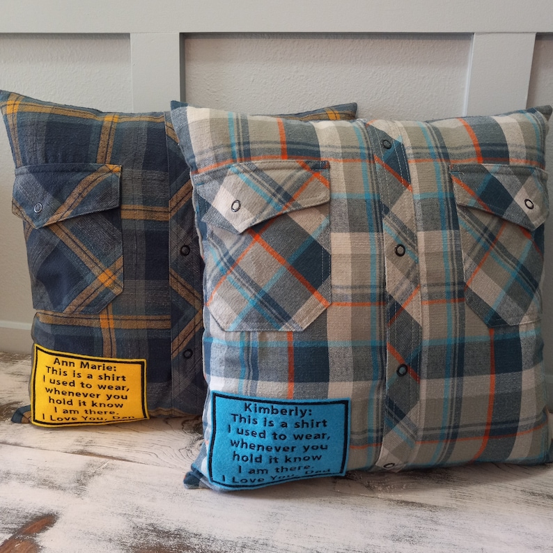 May include: Two cushions made from plaid shirts. One is blue and yellow, the other is grey, blue, and orange. Each cushion has a patch with text that reads, "This is a shirt I used to wear, whenever you hold it know I am there."