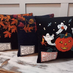 May include: Three decorative throw pillows. One black pillow features orange autumn leaves. Another black pillow has a navy background with fall leaves. The third black pillow has a Halloween theme with ghosts and a jack-o'-lantern. Each pillow has a printed message.
