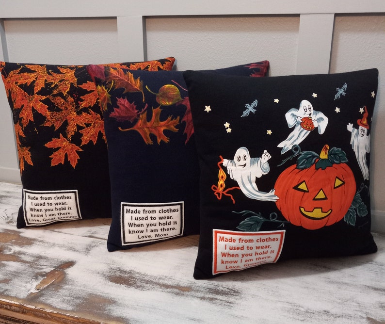 May include: Three decorative throw pillows. One black pillow features orange autumn leaves. Another black pillow has a navy background with fall leaves. The third black pillow has a Halloween theme with ghosts and a jack-o'-lantern. Each pillow has a printed message.