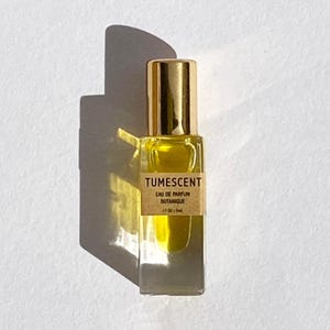 May include: A small perfume bottle with a gold cap and a clear glass body. The bottle contains a yellow liquid and has a label that reads "Tumescent Eau de Parfum Botanique". The bottle is 1.7 oz / 5ml.