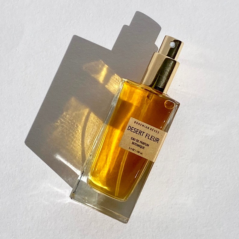 Close-up of Bohemian Rêves Desert Fleur Perfume Mist bottle casting deep red shadows, reflecting the warm, earthy essence of patchouli and vanilla. A bold, sun-drenched fragrance inspired by desert heat and golden light.