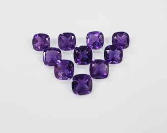 Könnte beinhalten: Eine Sammlung von zehn kissenförmigen Amethyst-Edelsteinen, die in Herzform auf einem weißen Hintergrund angeordnet sind.