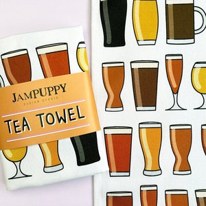 May include: White tea towel featuring a colourful pattern of different beer glasses and mugs. The text "JAMPUPPY DESIGN STUDIO" and "TEA TOWEL" is printed on the towel.