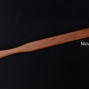 May include: A long, wooden paddle with a rounded handle. The paddle is a reddish-brown color and has a smooth finish. The text "Niove" is printed on the paddle.