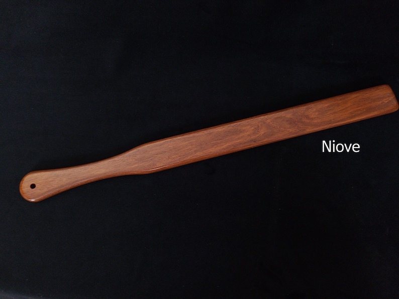 May include: A long, wooden paddle with a rounded handle. The paddle is a reddish-brown color and has a smooth finish. The text "Niove" is printed on the paddle.