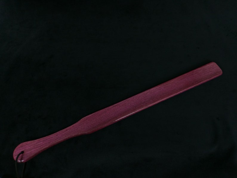May include: A long, wooden paddle with a rounded end. The paddle is a deep purple color and has a smooth, polished finish.