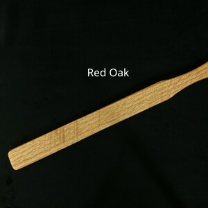 May include: A wooden paddle made of red oak. The paddle is approximately 18 inches long and has a rounded end.