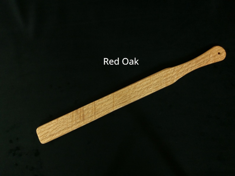 May include: A wooden paddle made of red oak. The paddle is approximately 18 inches long and has a rounded end.