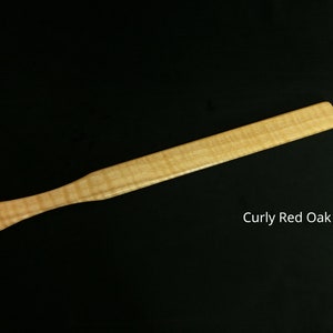 May include: A long, thin, wooden paddle made of curly red oak. The paddle has a rounded handle and a flat, rectangular blade.